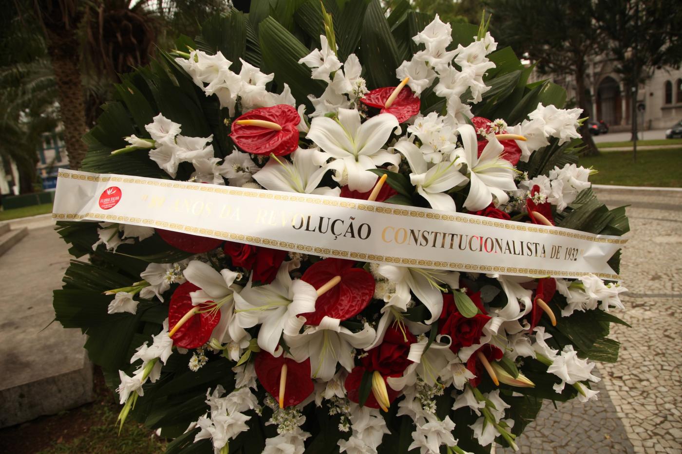 #pracegover coroa de flores na praça tem faixa com a inscrição Revolução Constitucionalista