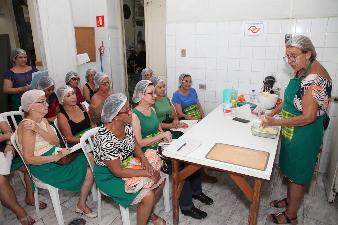 professora mostra a alunas sentadas materiais de curso #paratodosverem