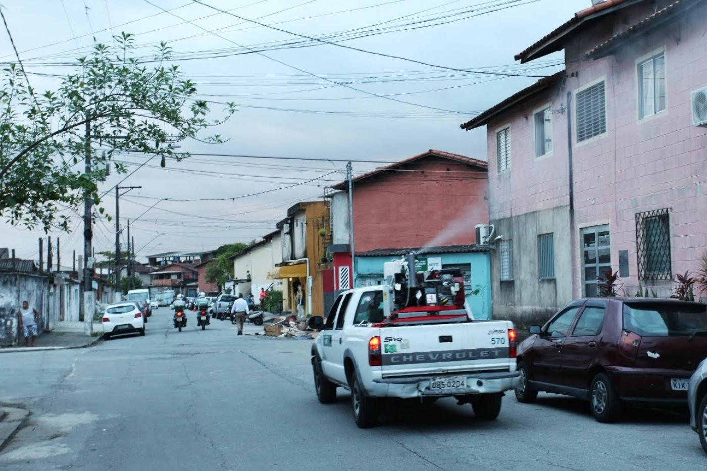 Carro fumacê percorre rua e lança fumaça para o lado direito. #Paratodosverem