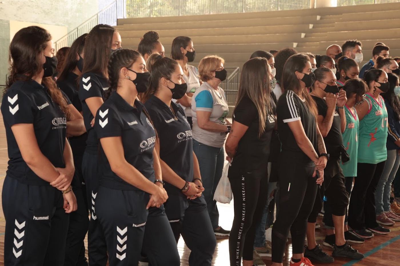 Atletas no ginásio acompanham cerimônia #paratodosverem