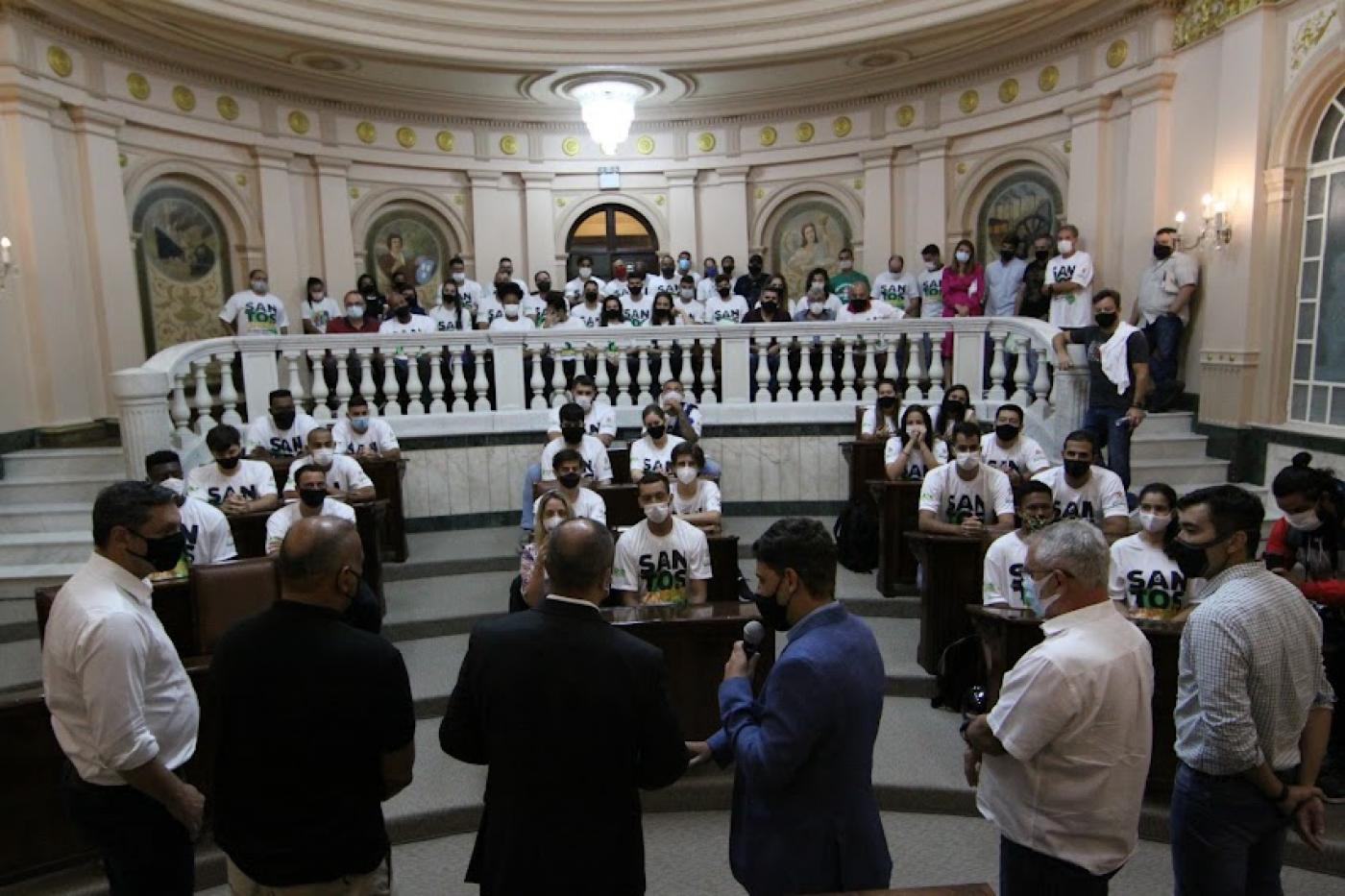 Autoridades discursam em pé para atletas sentados na galeria da Sala Princesa Isabel. #pracegover