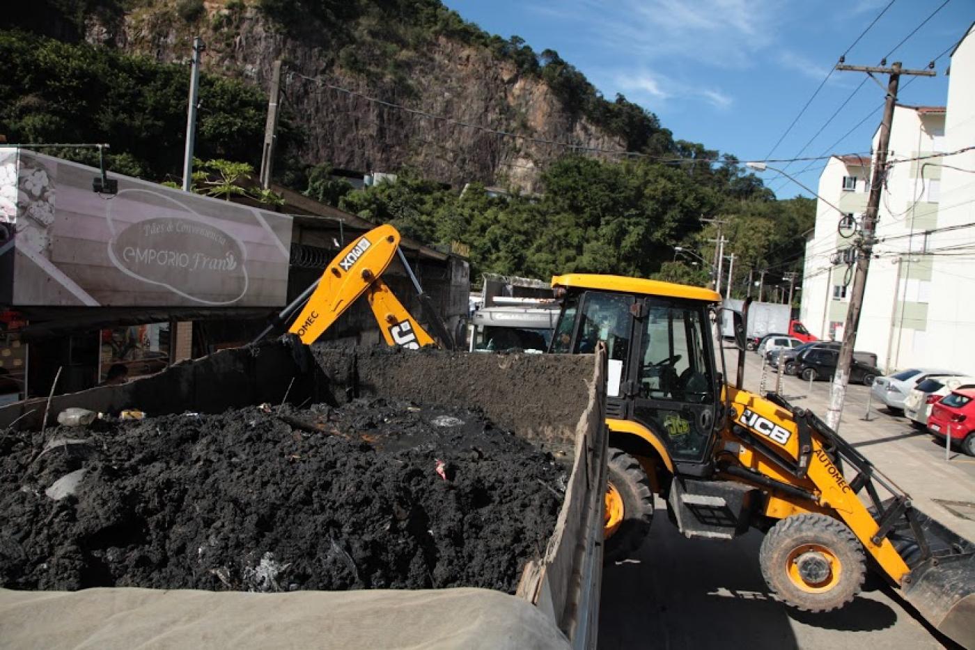 trator está ao fundo e ao lado de uma caçamba onde está depositado grande volume de resíduos. #paratodosverem 