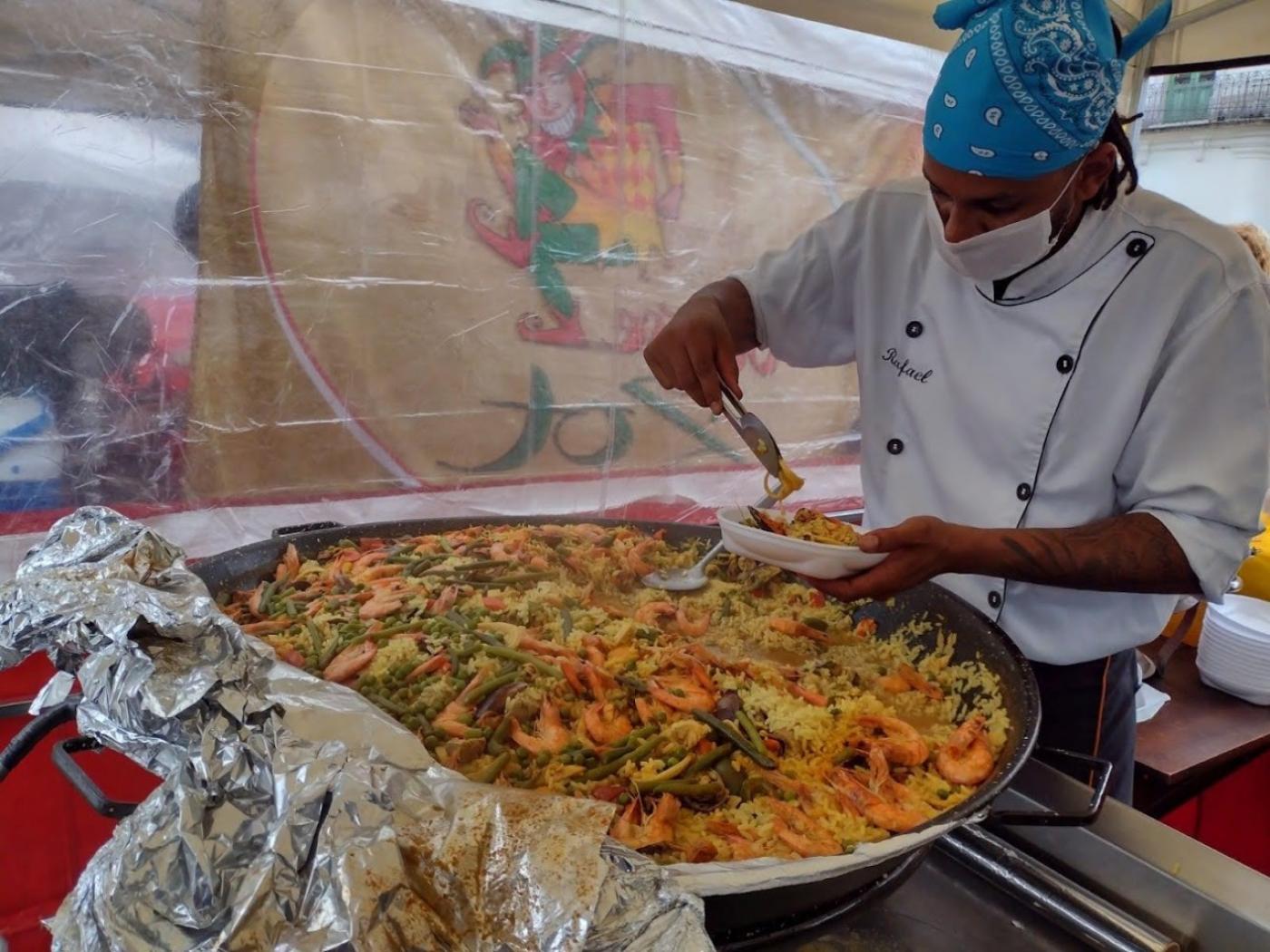 Cozinheiro, paramentado, retira alimentos de grande panela e coloca em prato. #paratodosverem