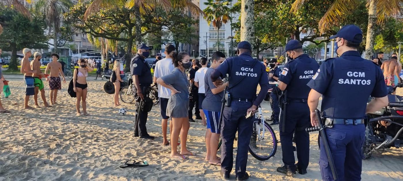 guardas municipais estão em torno de pessoas na faixa de areia. #paratodosverem