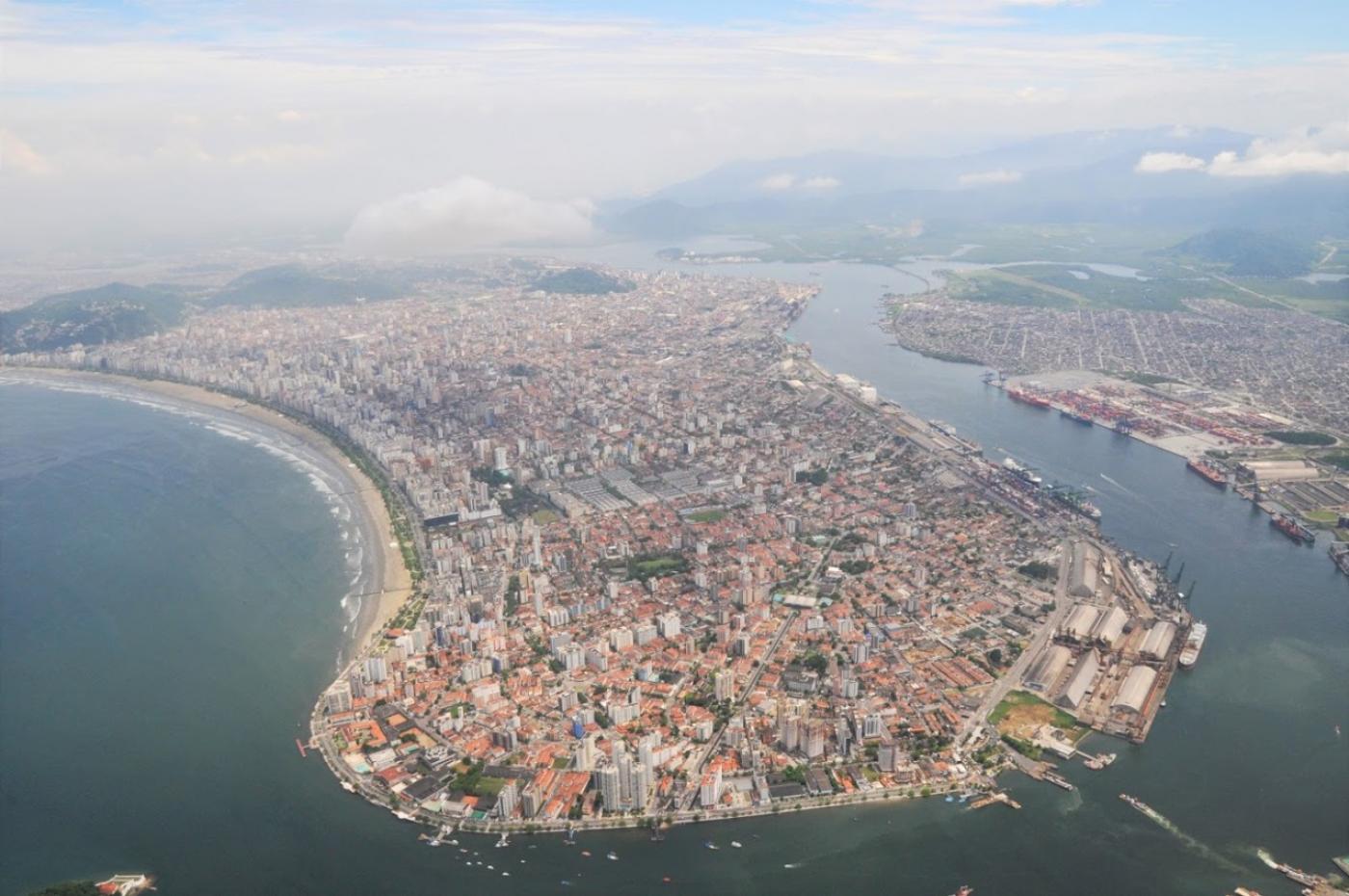 Vista panorâmica da cidade onde se vê a ilha contornada por mar, toda a extensão do porto e, do outro lado, da orla. #Paratodsoverem