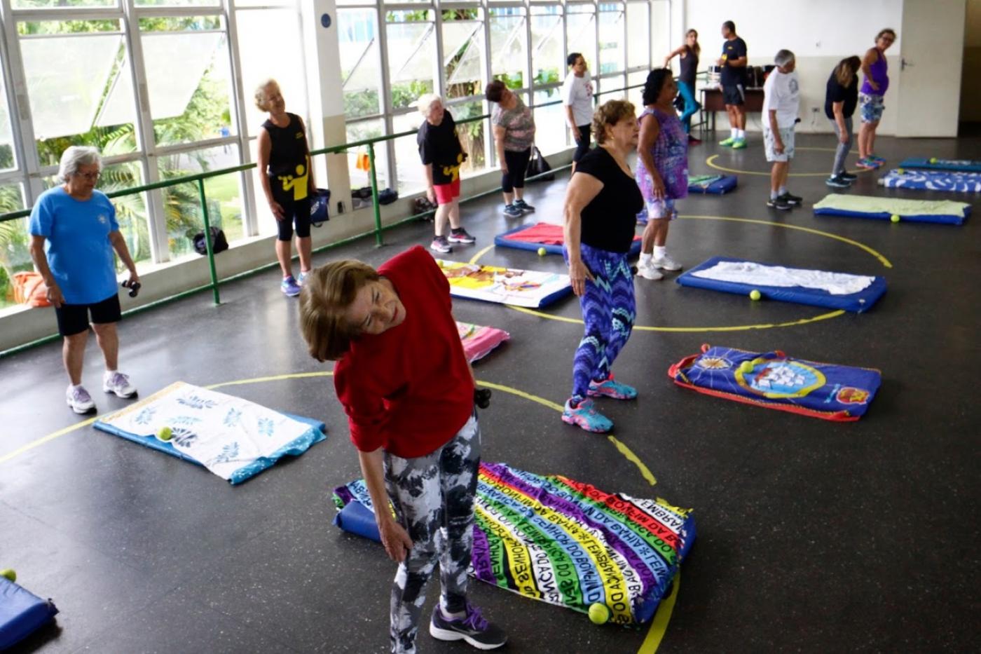 MULHERES ESTÃO FAZENDO EXERCÍCIO EM PÉ, AO LADO DE COLCHONETES. #PARATODOSVEREM