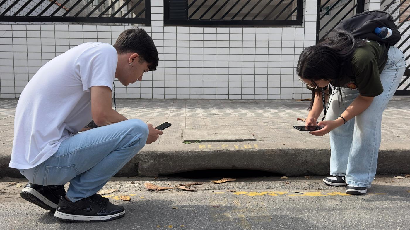 dois jovens observam buraco em rua. #paratodosverem 
