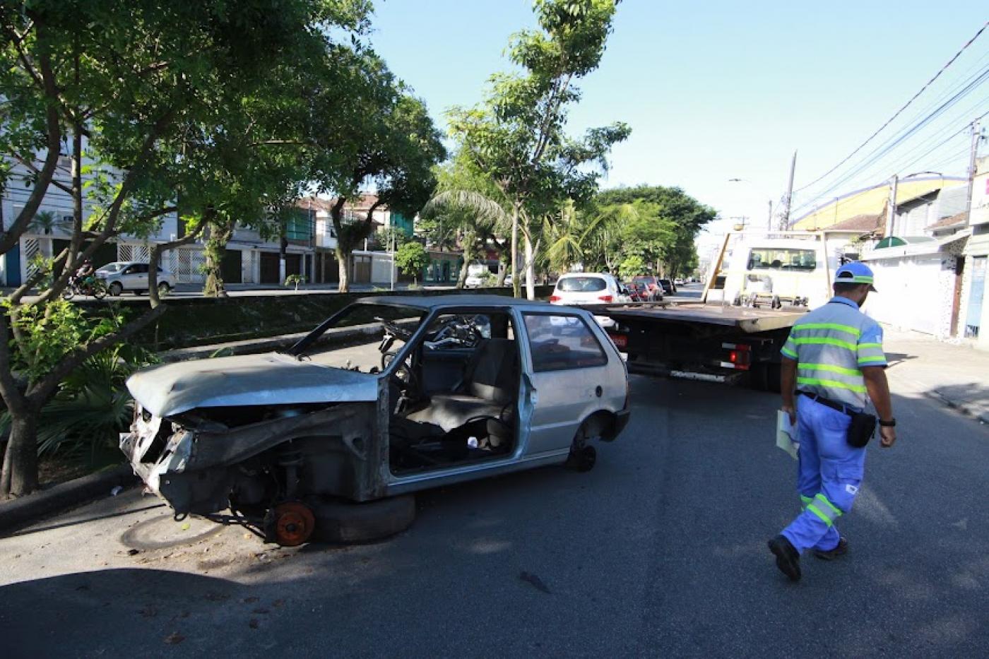 veículo parcialmente destruído é guinchado em avenida. Canal está ao lado. Agente da CET está do outro, na pista. #paratodosverem