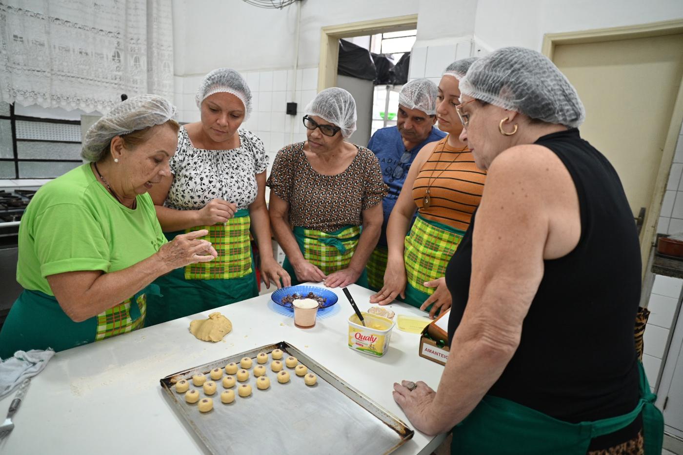 mulheres assistem a produção de biscoitos artesanais. #paratodosverem