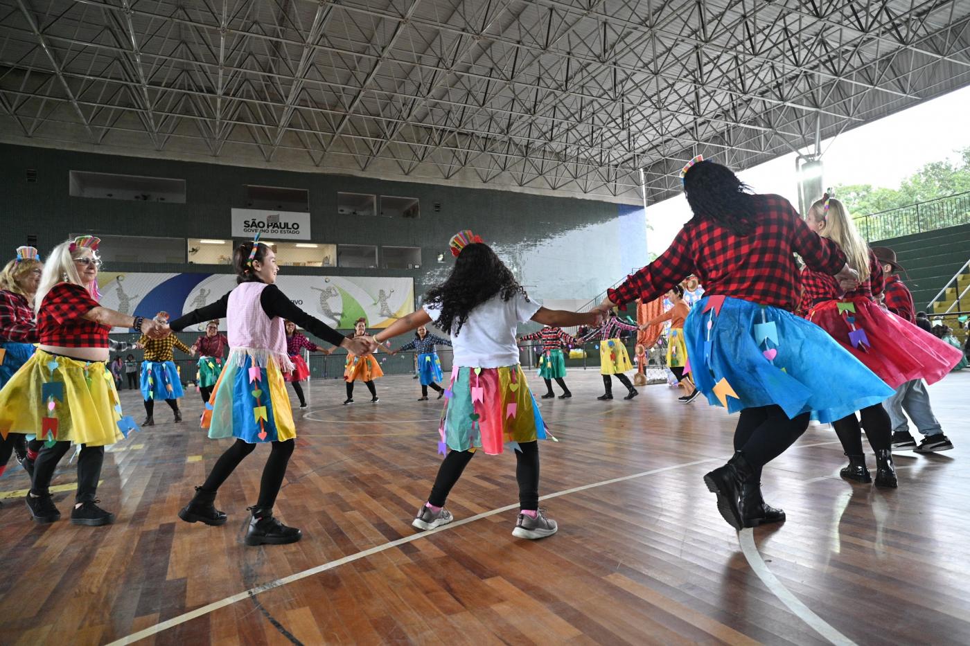 pessoas com roupas juninas dançam em roda. #paratodosverem