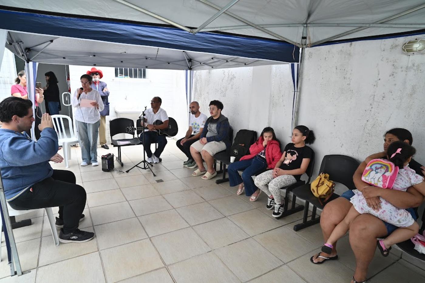 mulher em pé se apresenta para público sob tenda. #paratodosverem 