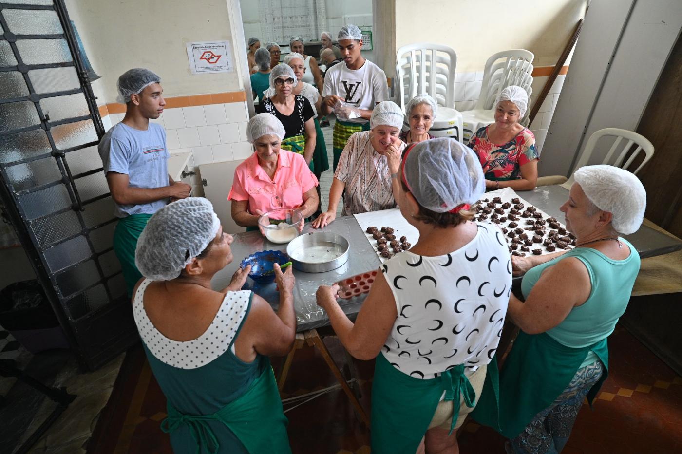 pessoas reunidas em torno de mesa fazendo bombons. #paratodosverem