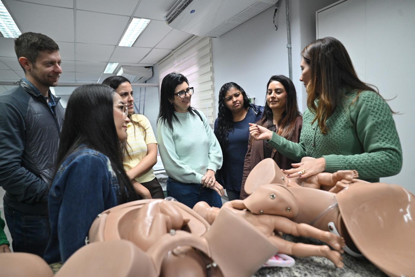 mulher orienta profissionais diante de modelos de borracha. #paratodosverem