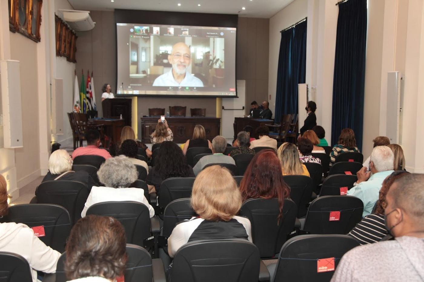 Homem fala em telão para pessoas em auditório #paratodosverem