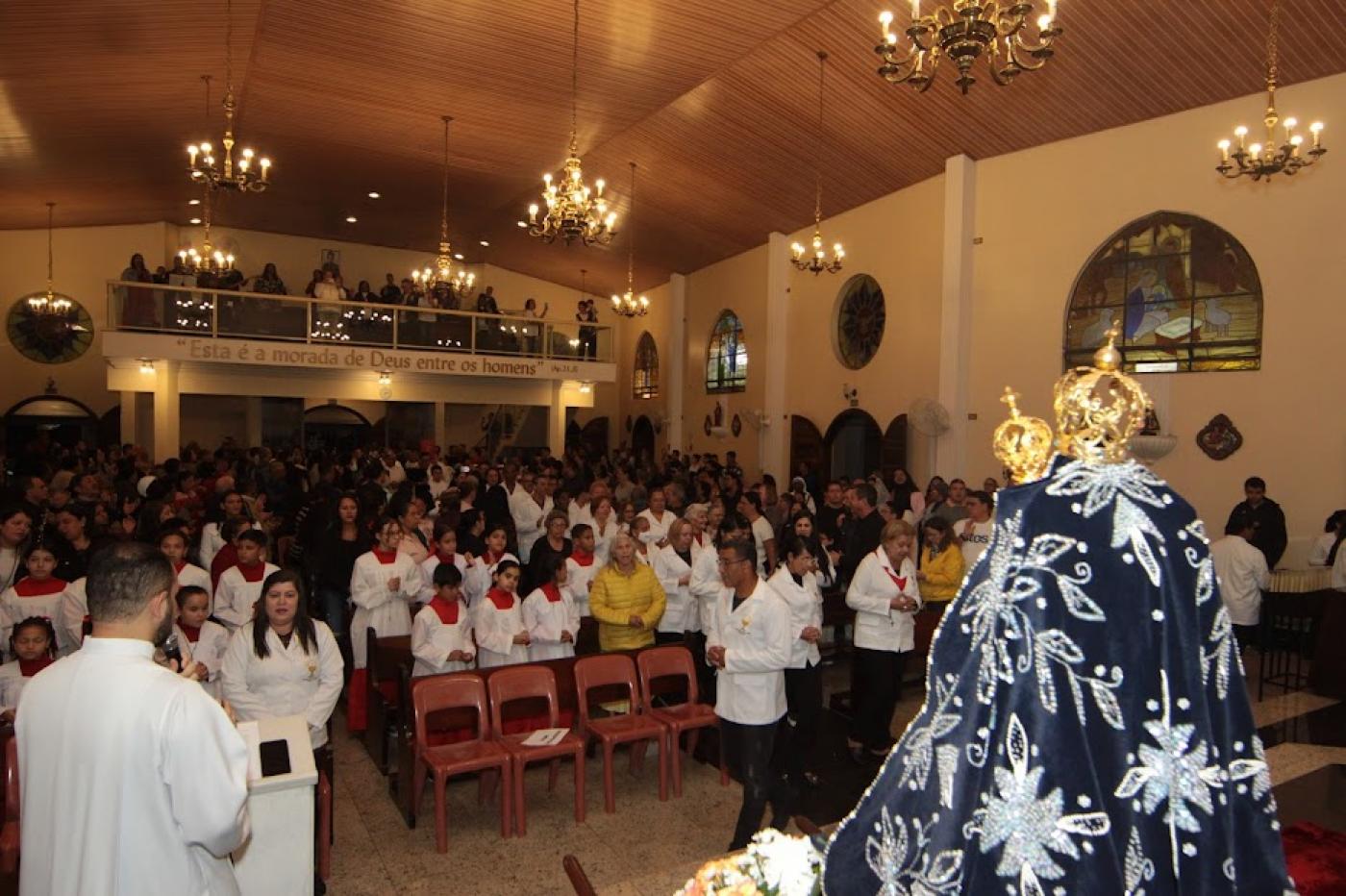 Igreja lotada de fiéis coma imagem da Santa em primeiro plano.