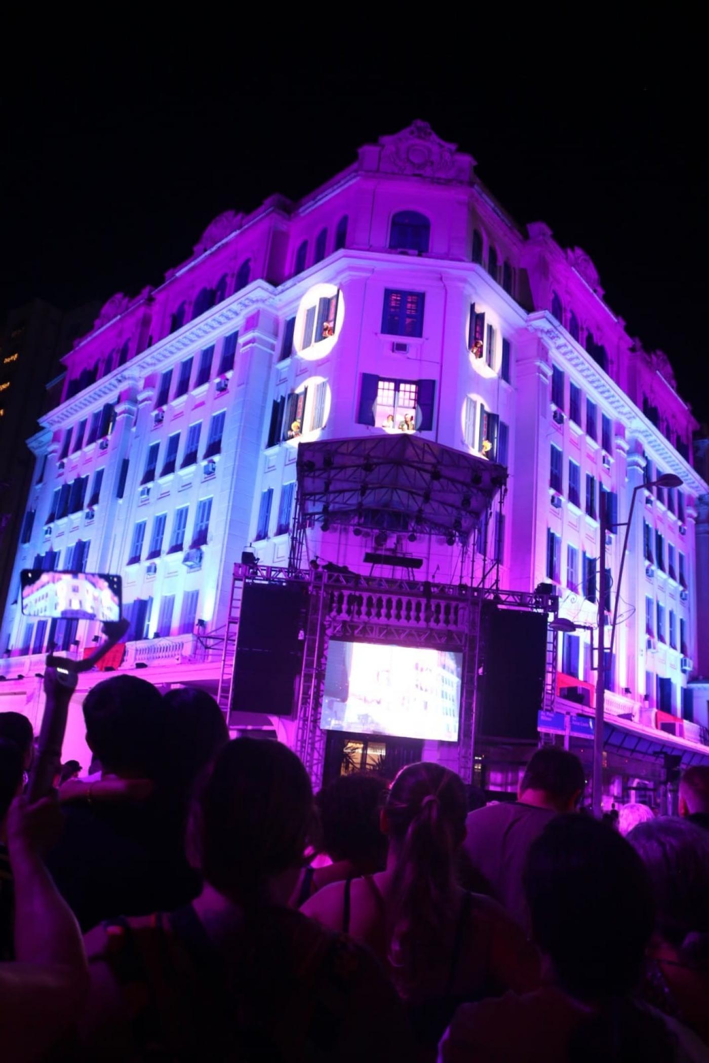 Fachada do hotel iluminada com palco à frente. #paratodosverem