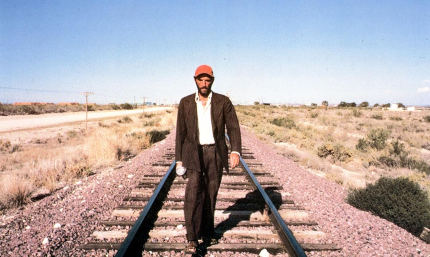 Homem caminha sob trilho de trem em área deserta