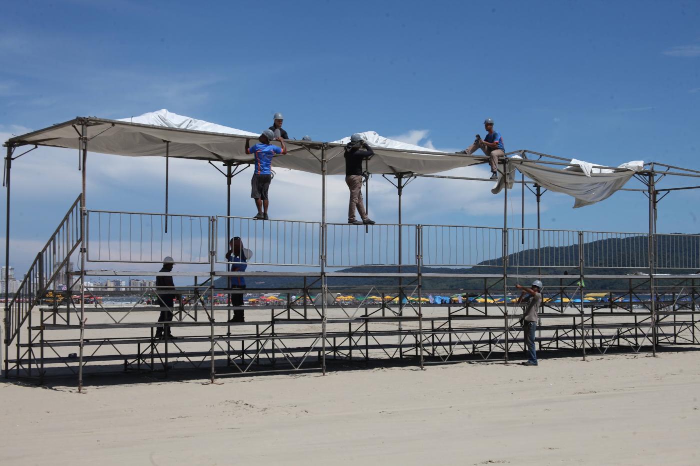 homens montam estrutura de arquibancada sobre a areia. #paratodosverem 