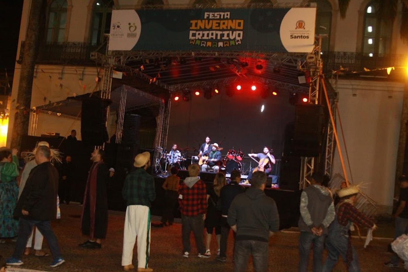 pessoas estão assistindo aprensentação em palco ao fundo. #paratodosverem