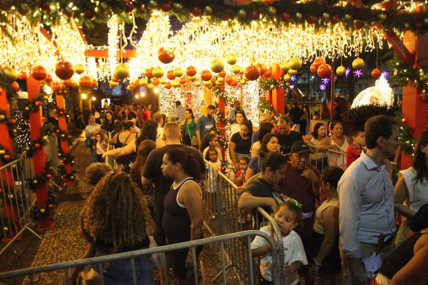 púbico lota praça mauá sob luzes decorativas de natal. Fila para entrar na casinha do papai noel. #paratodosverem 