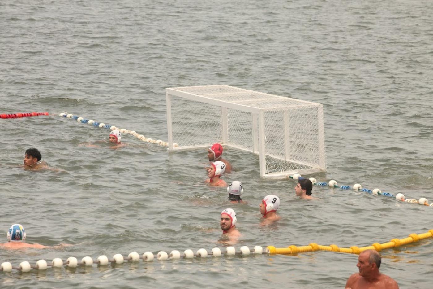 quadra de polo aquático no mar, com atletas na água e a trave no fundo. #paratodosverem 