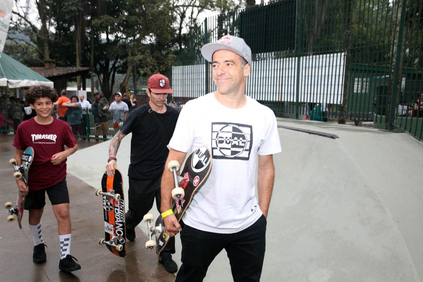 À frente da pista, Mineirinho posa com skate na mão e dois adolescentes atrás