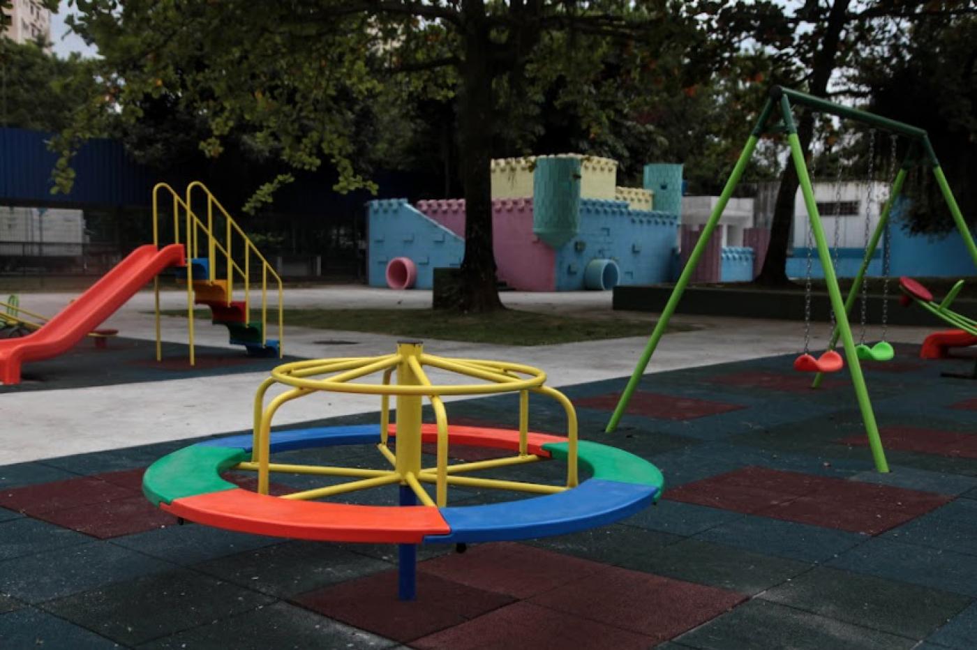 parque infantil com gira-gira em primeiro plano, balancês à direita, escorredor à esquerda e um castelinho ao fundo. #paratodosverem 