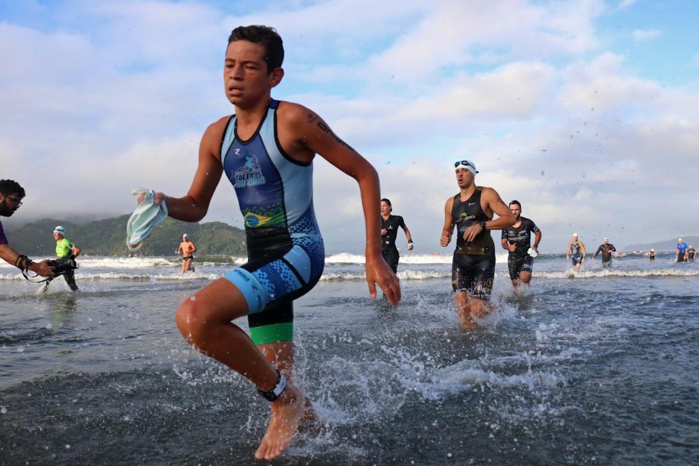 jovem está saindo da água, na beira do mar, encerrando prova aquática. #paratodosverem