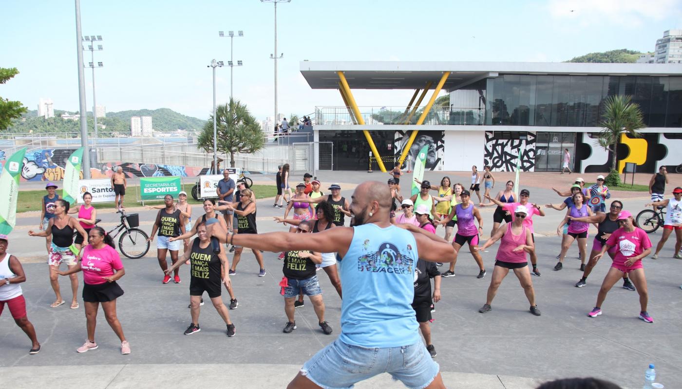 professor faz movimento que é repetido pelo público ao fundo. #paratodosverem 