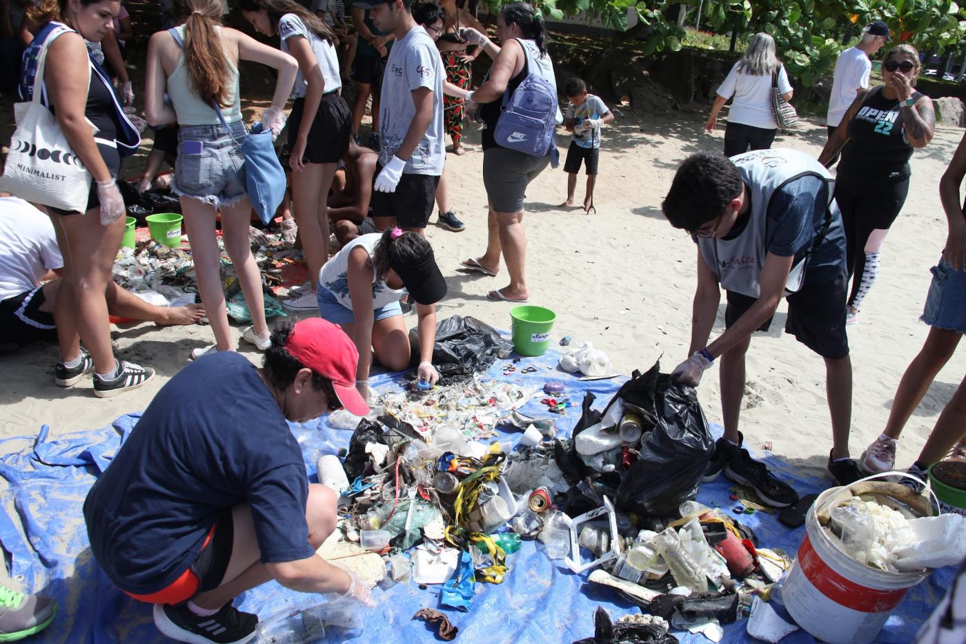 pessoas selecionam lixo coletado e separado sobre areia. #paratodosverem