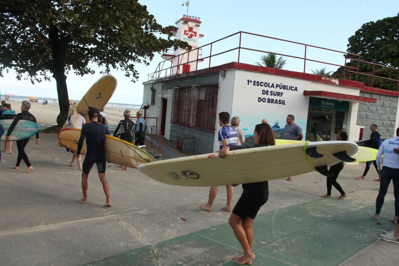 fachada da escola de surfe com alunos segurando pranchas. #paratodosverem