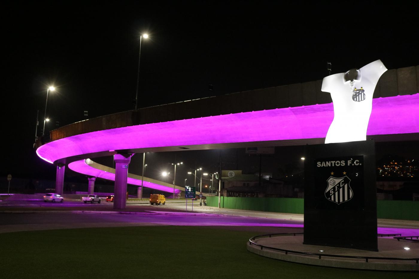 viaduto na entrada da cidade com iluminação cor-de-rosa. Monumento da camisa do rei pelé à direita. #paratodosverem