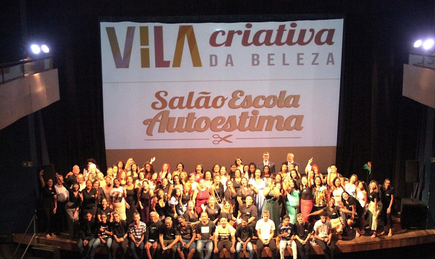 turma de formando se junta em palco para foto. ao fundo um grande banner onde se lê Vila Criativa da Beleza salão escola Autoestima