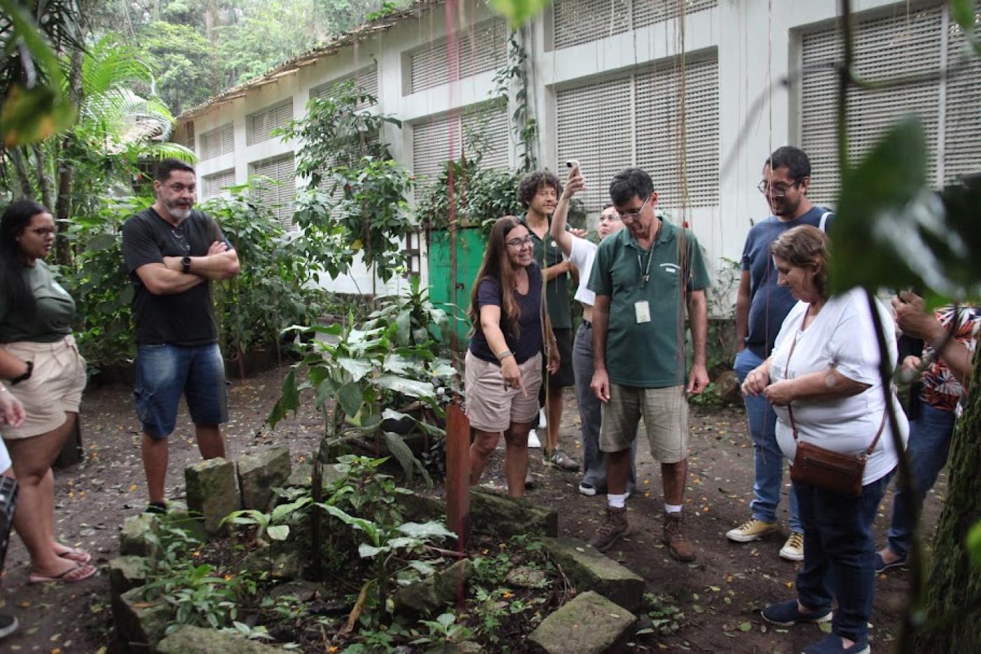 grupode pessoas está em volta de uma composta e uma área verde. #paratodosverem 