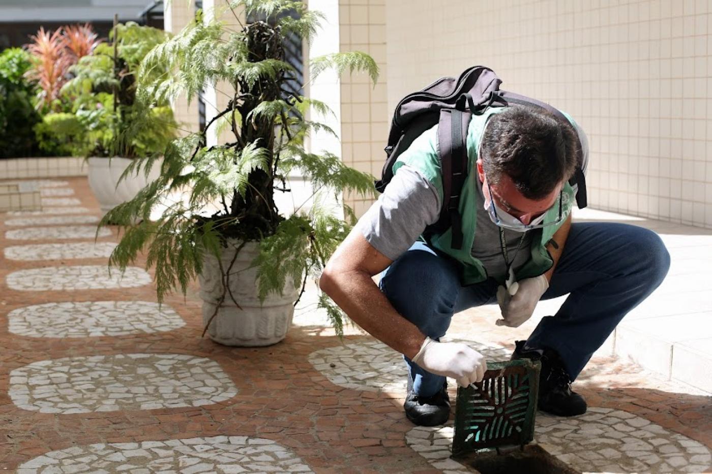 agente está agachado junto a ralo que ele abriu para observar na parte interna. #paratodosverem