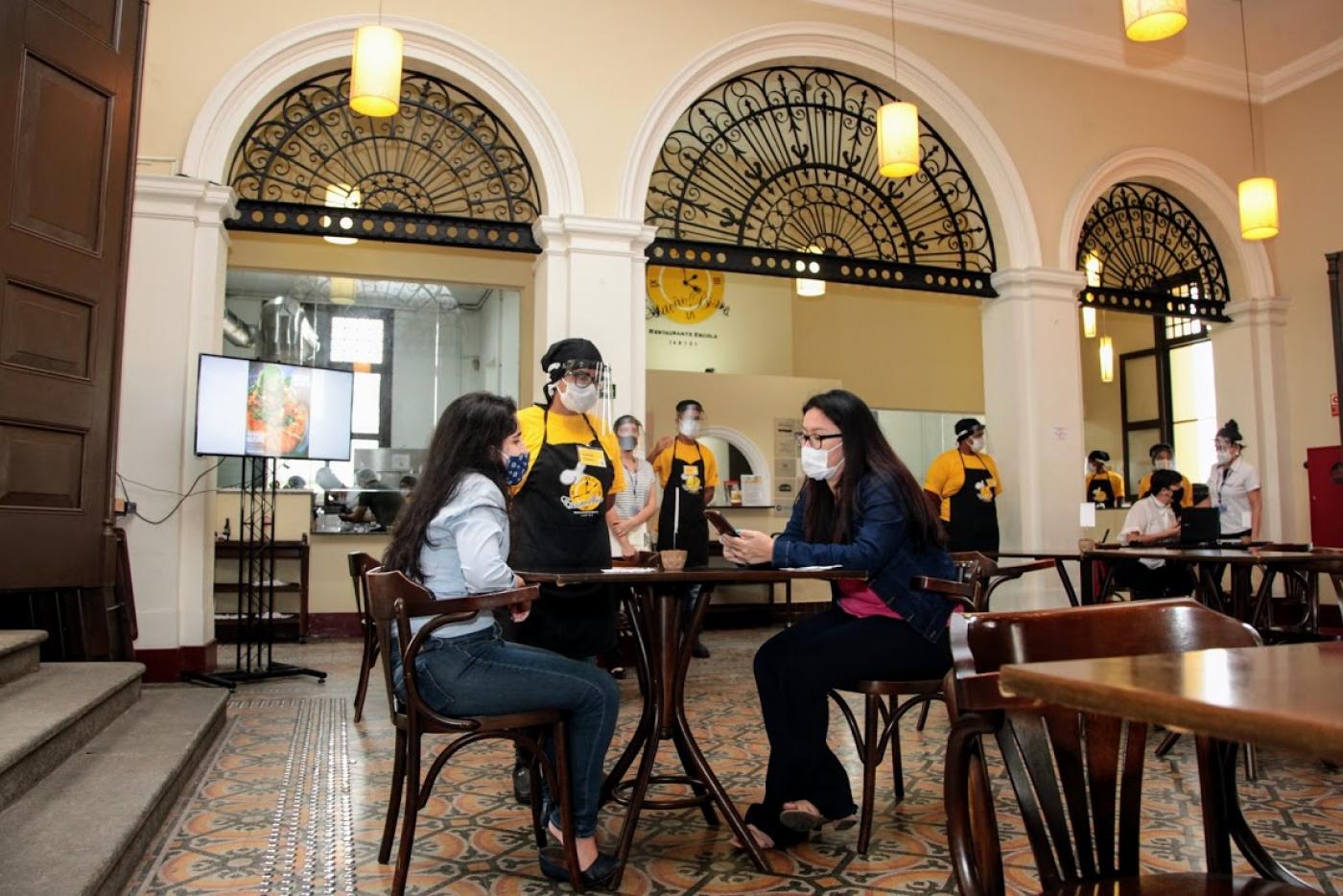 garçonete atende mesa com duas mulheres #paratodosverem