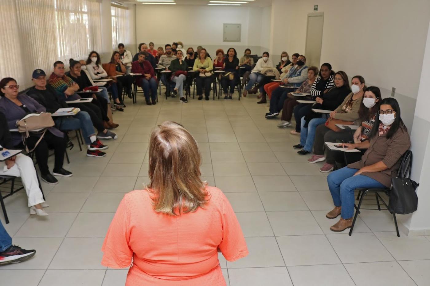 pessoa falando para diversas pessoas sentadas em forma circular. #paratodosverem