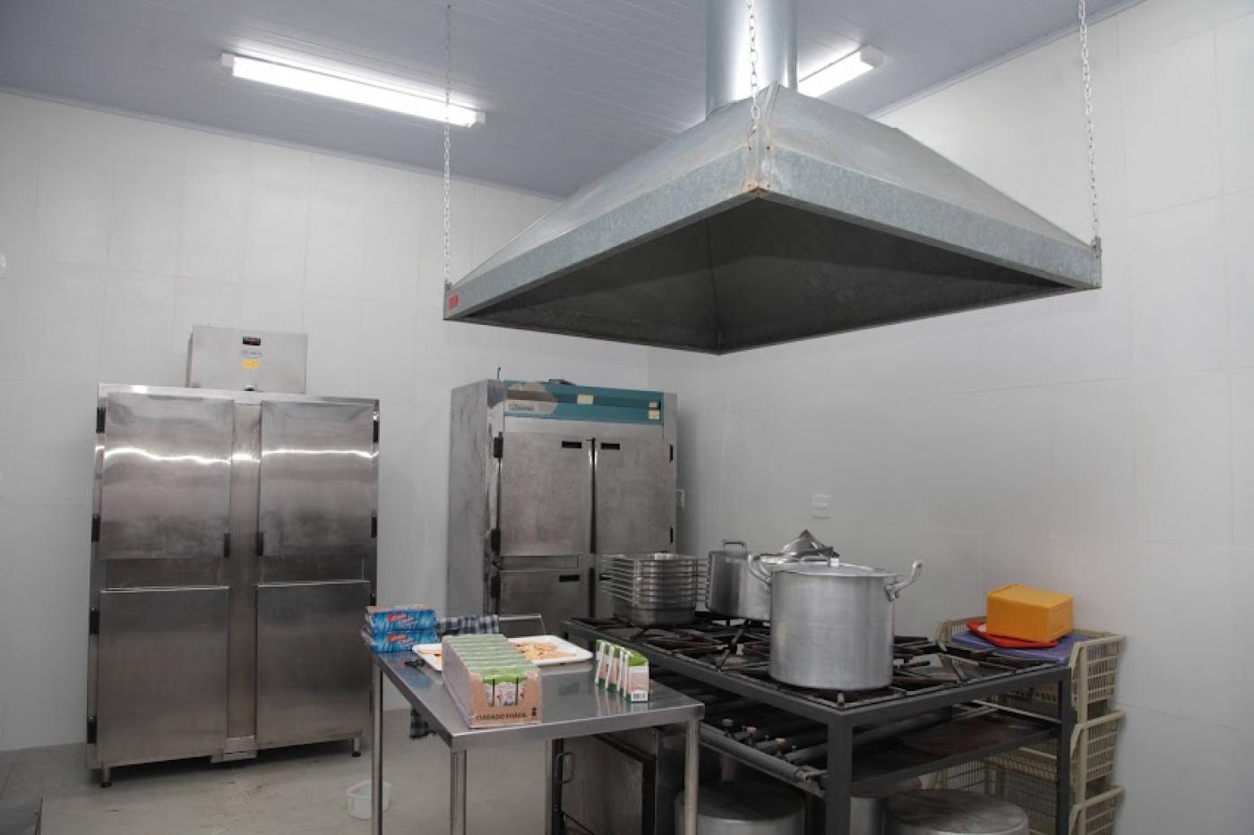 cozinha com fogão industrial, coifa, mesa e geladeiras. #paratodosverem
