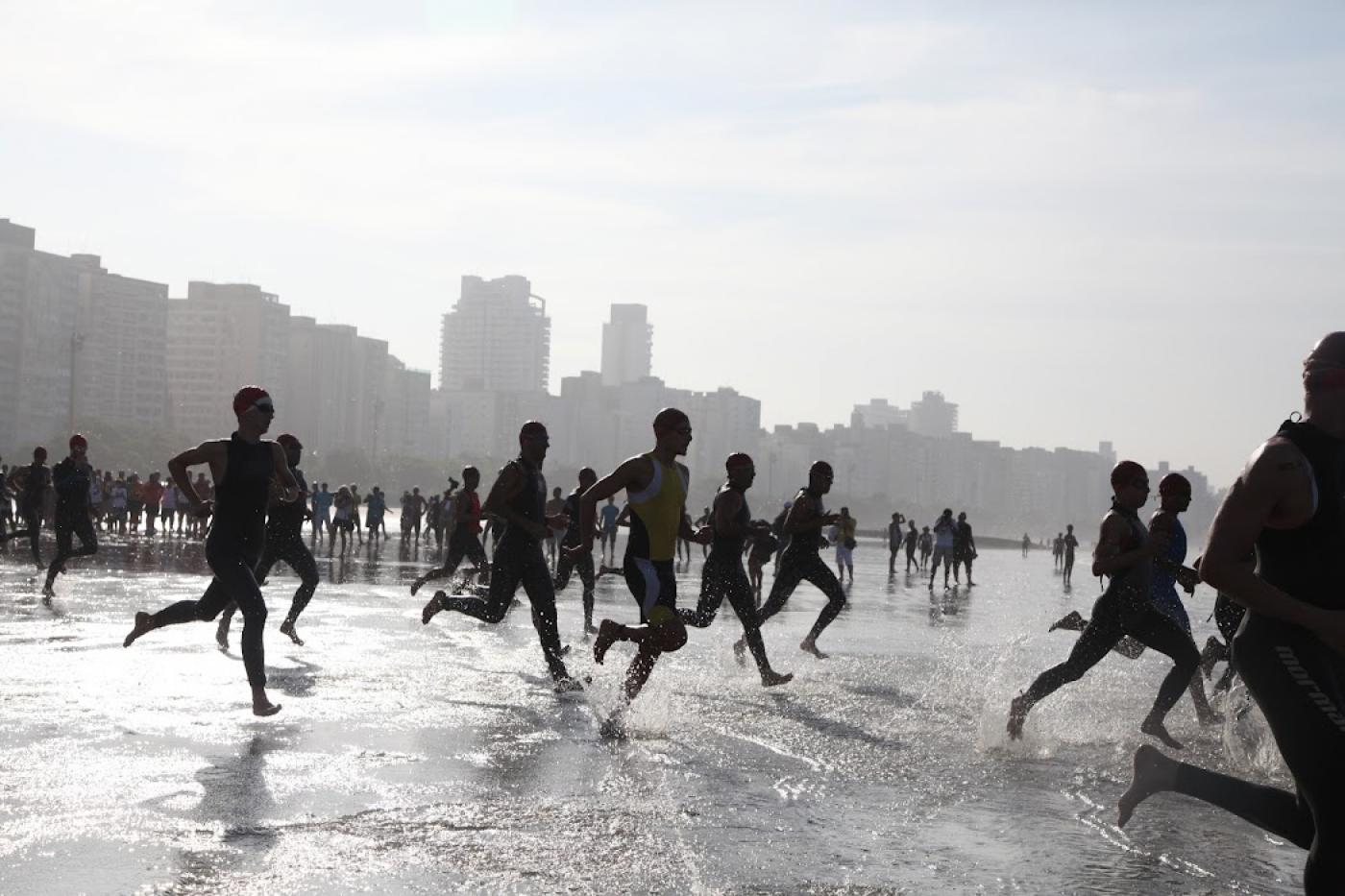 Pessoas correndo na direção do mar em competição #paratodosverem
