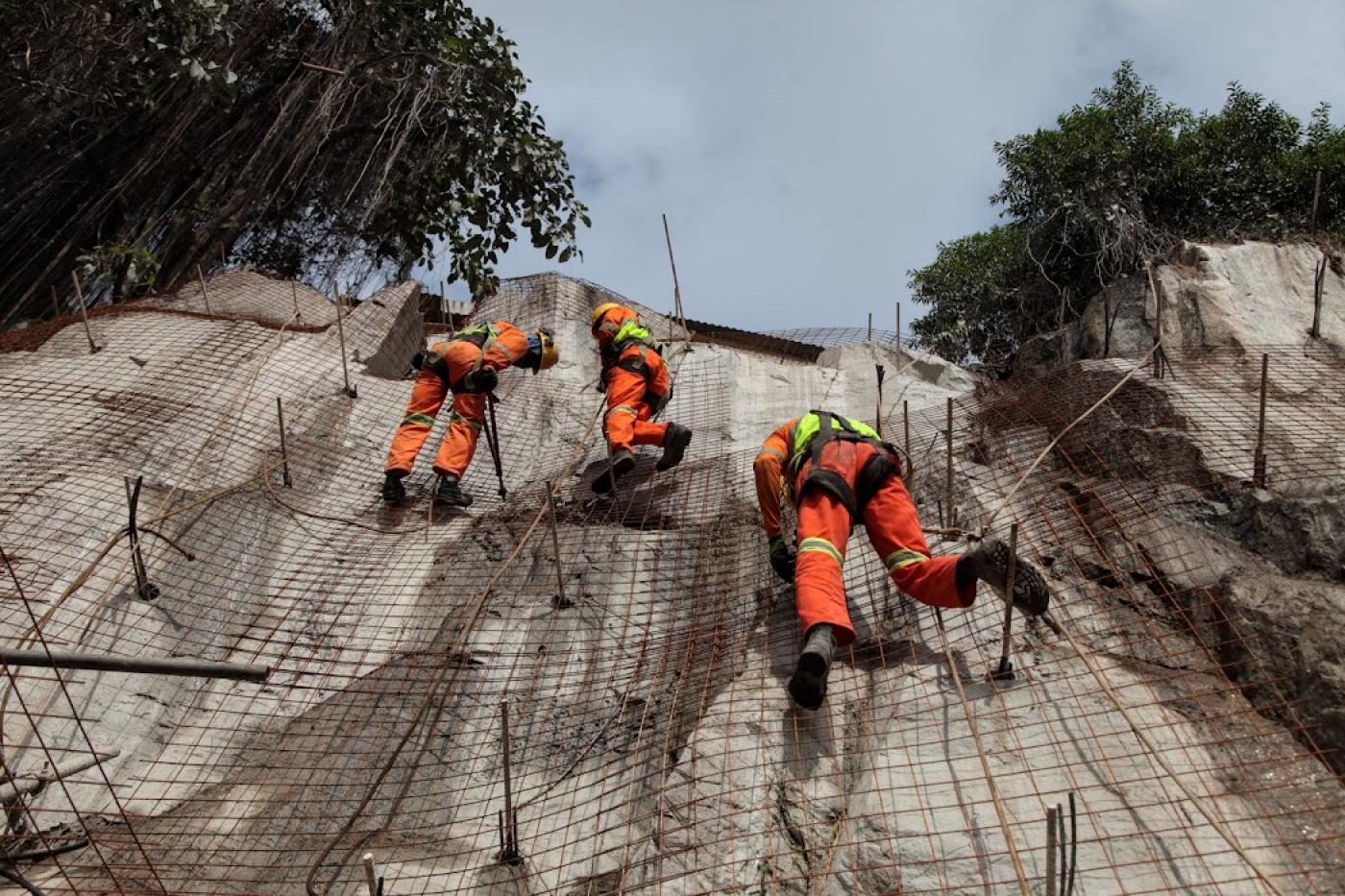 profissionais escalando encosta de morro durante obra #paratodosverem