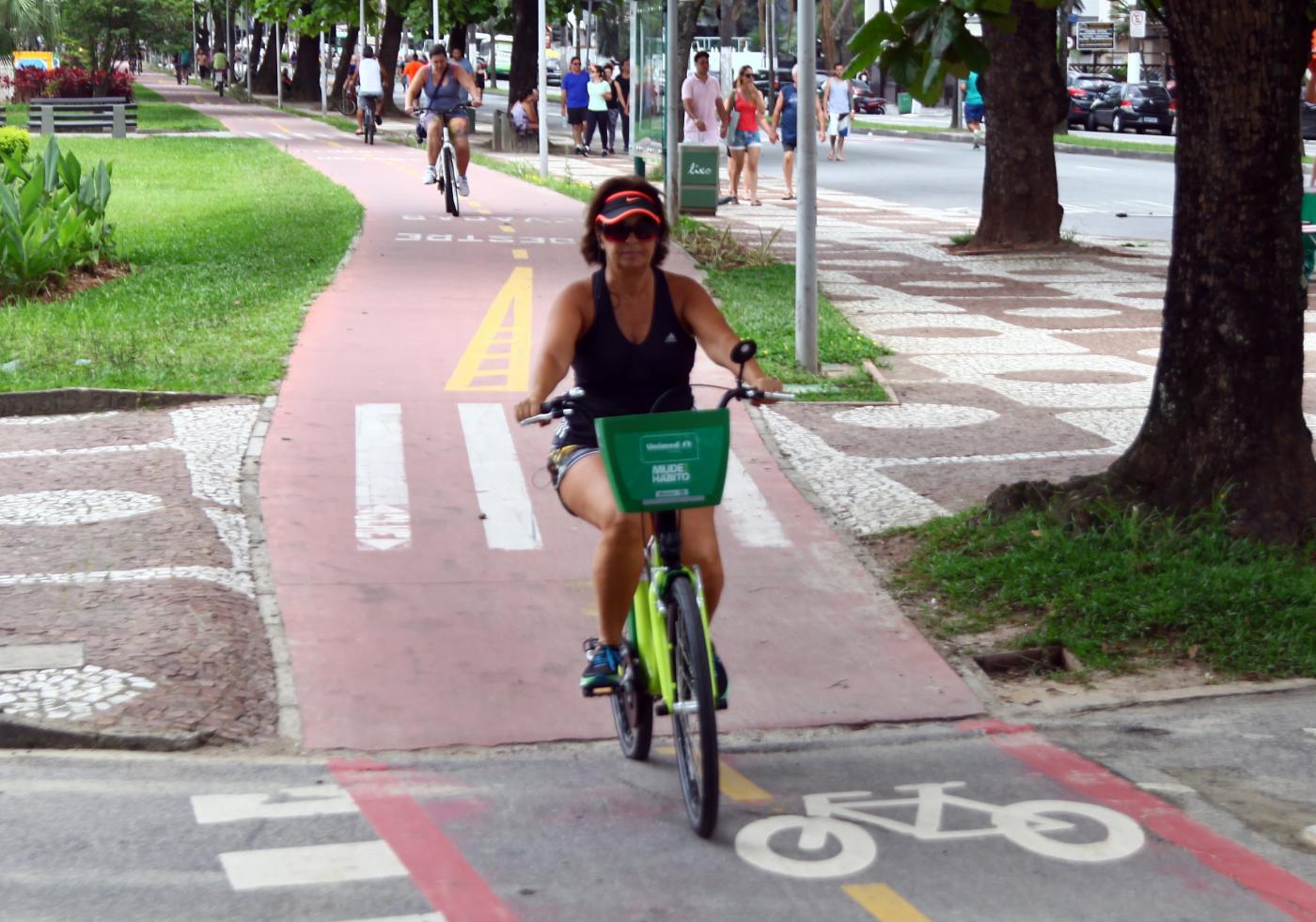 Mulher está pedalando bicicleta do bike santos em ciclovia. #Pracegover