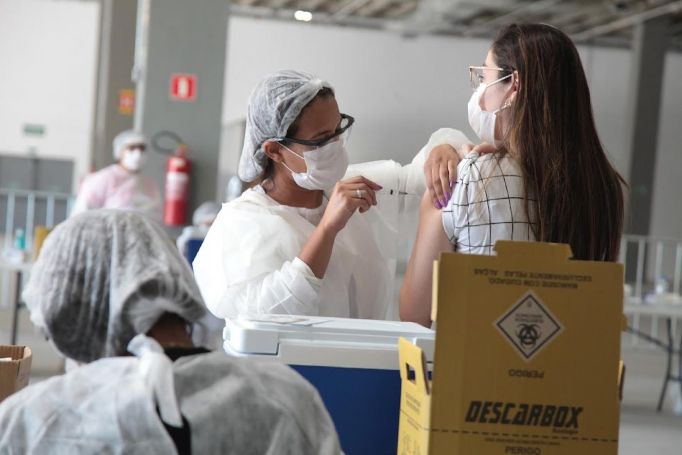 Enfermeira aplica vacina no braço de mulher. #paratodosverem