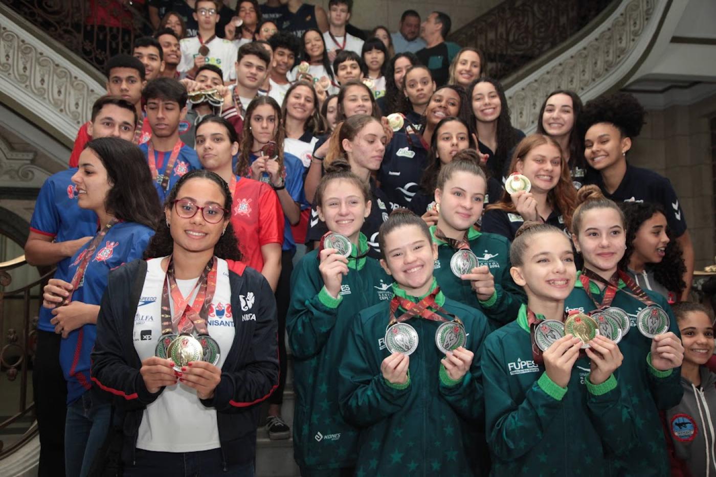 vários atletas exibem medalha em escadaria #paratodosverem