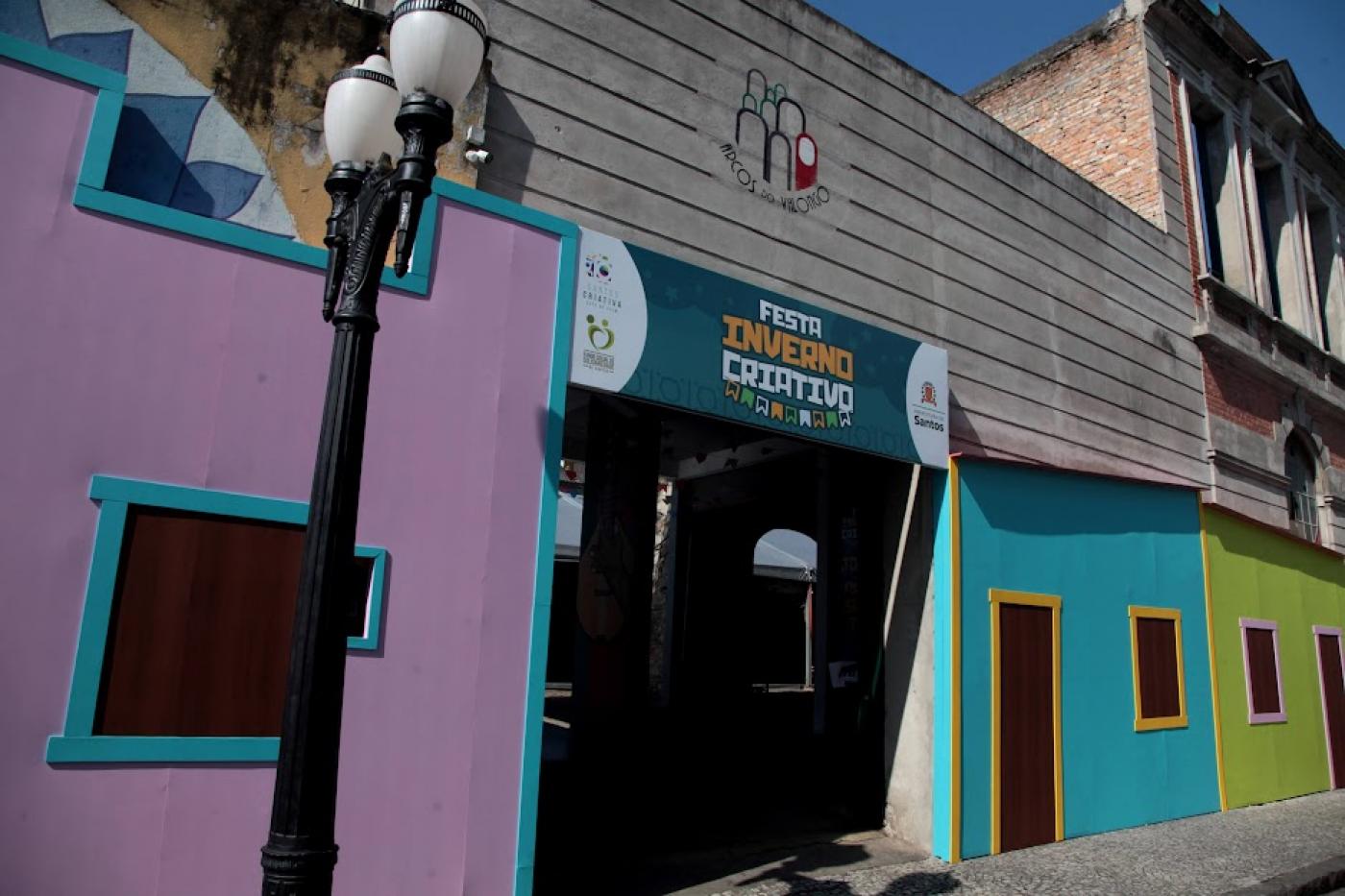 fachada de prédio colorida e placa no alto da entrada onde se lê Festa Inverno Criativo. #paratodosverem 