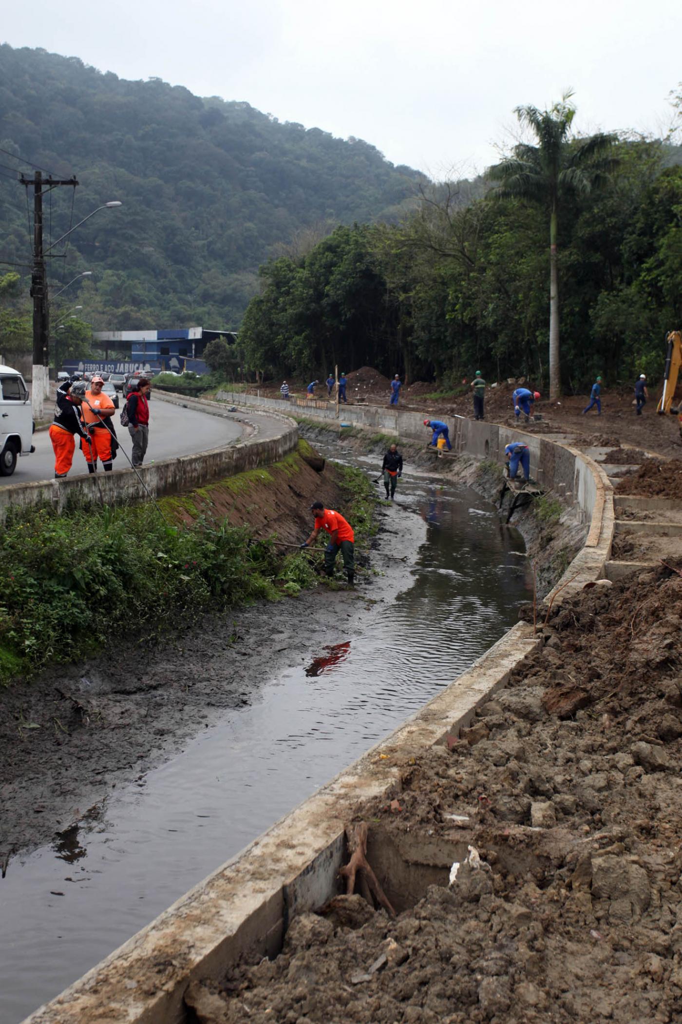 Canal de avenida com talude em manutenção e desassoreamento. # Pracegover