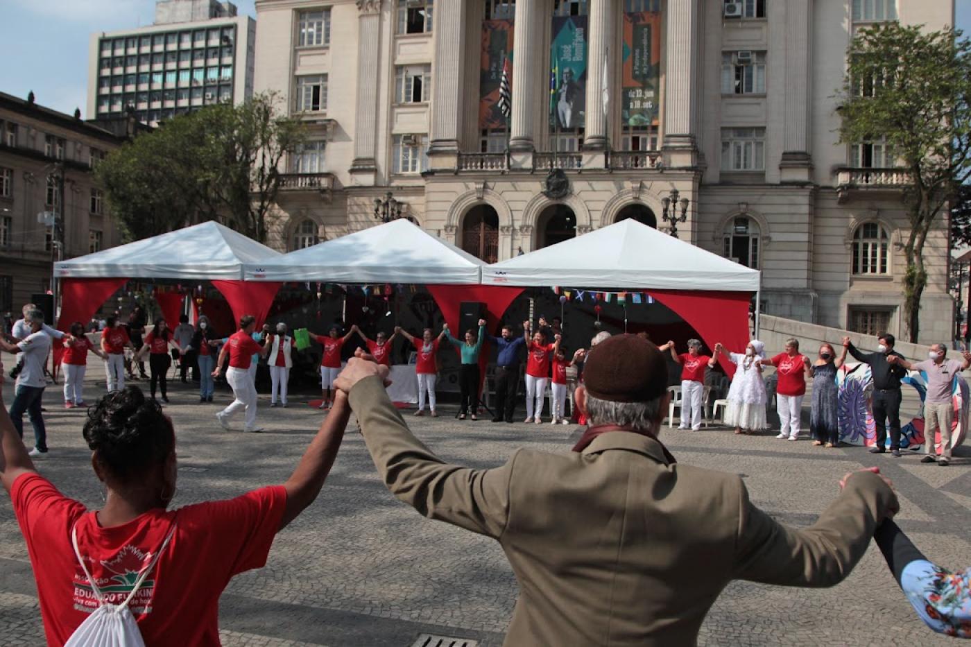 pessoas de mãos dadas e para cima em circulo na praça #paratodosverem