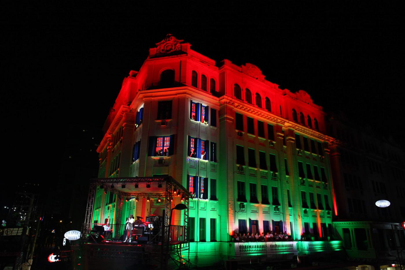 Fachada de hotel iluminada em vermelho e verde, cores típicas do Natal, para show musical. #Pracegover