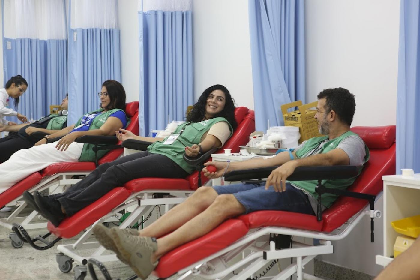 agentes de combate a endemias uniformizados estão em macas doando sangue. Na imagem se vê quatro doadoras e uma mulher atendendo um deles. #paratodosverem 
