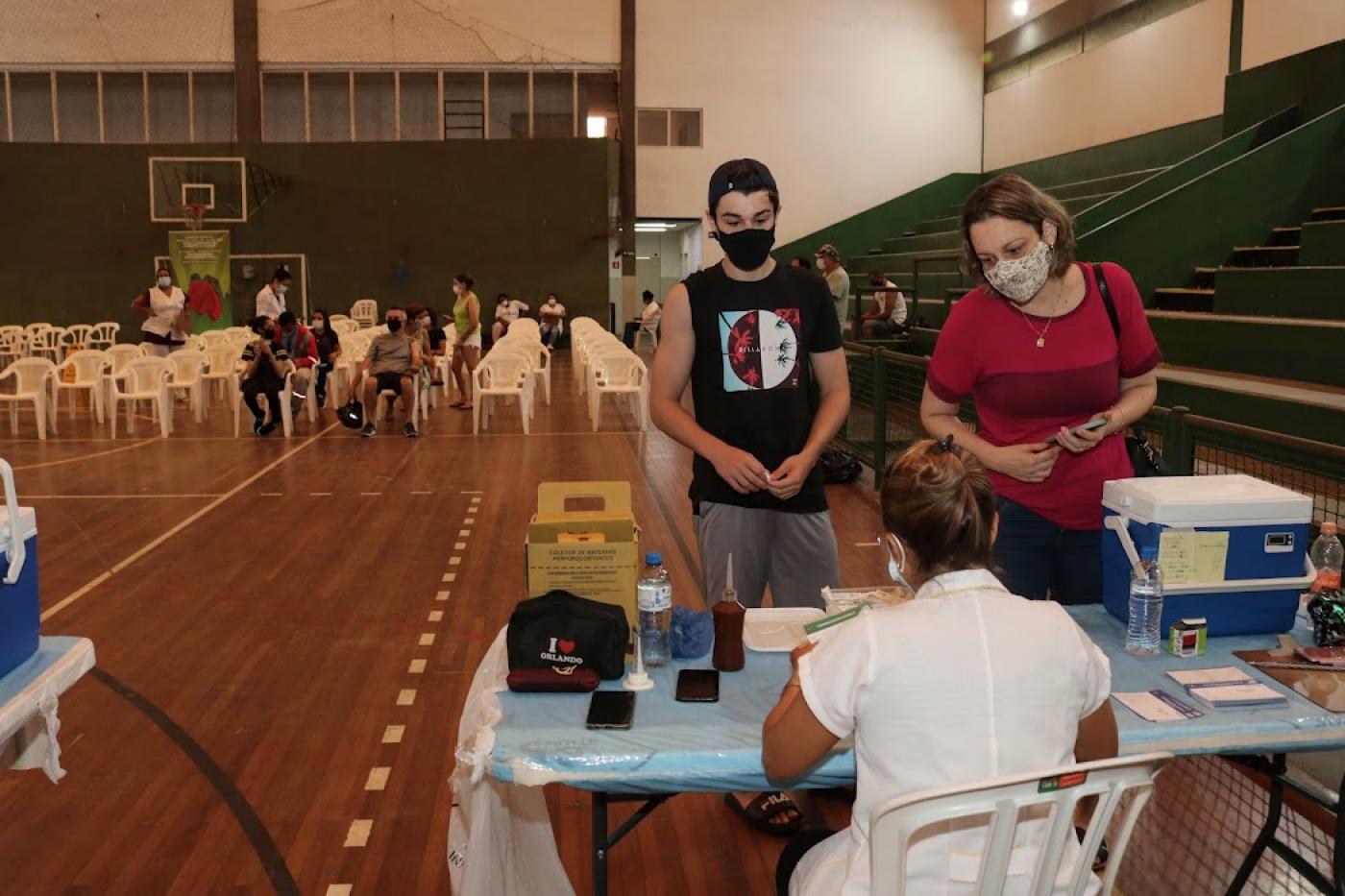 jovem e mulher são atendidos em ginásio para vacinação #paratodosverem