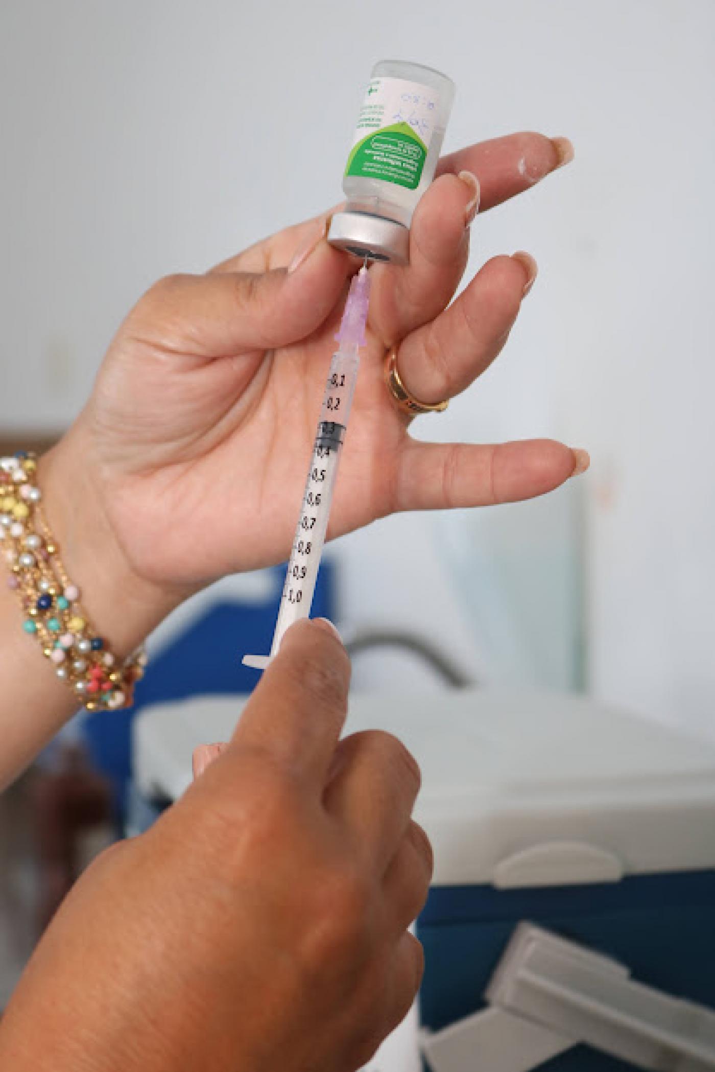 mãos seguram seringa com agulha espetada em frasco de vacina. #paratodosverem